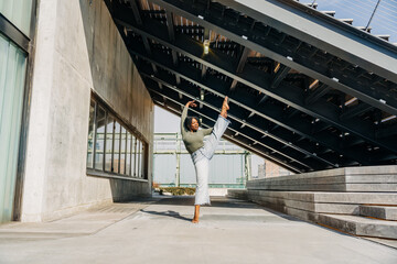 Dancer lifts leg high in pose under modern urban structure