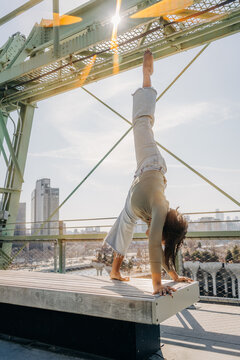 Woman holding handstand on platform under bright urban sunlight