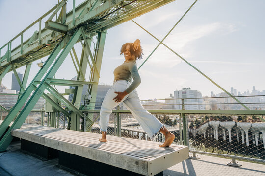 Smiling woman striking a pose on a bench with city backdrop