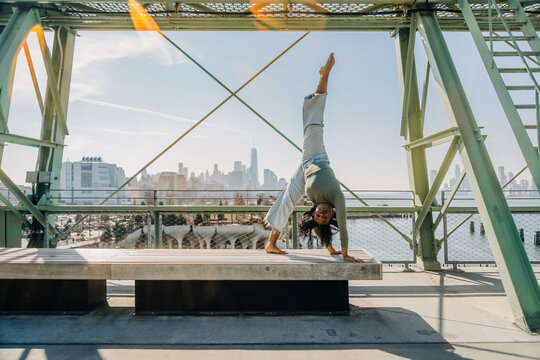 Woman performs handstand on bench with NYC skyline behind her