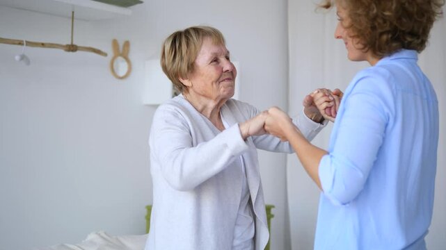 Professional caregiver helping happy senior woman to stand up from sofa at home, assisting her in her daily life and providing support, showing compassion and care