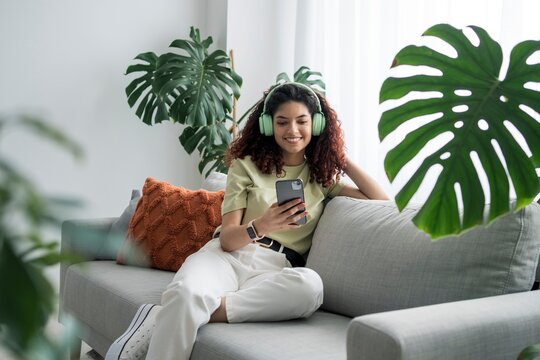 Woman relaxing on a sofa with headphones and smartphone indoors