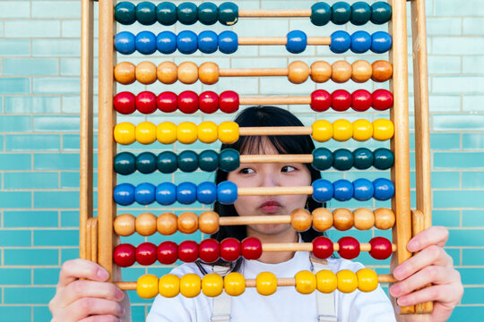 Woman with multi colored abacus puckering in front of brick wall