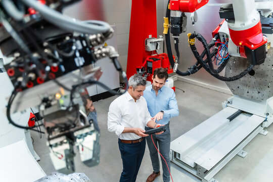 Male engineers discussing over control while machinery in foreground at factory