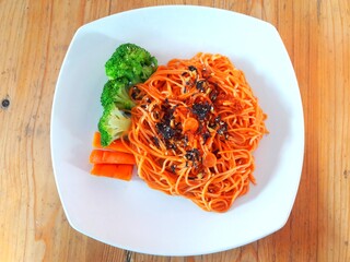 Healthy menu consisting of spaghetti and boiled carrots and broccoli served on white plates, on wooden tables.