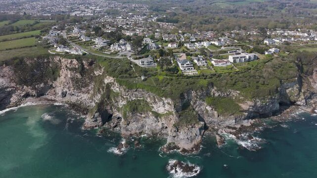 Aerial view of modern cliff-edge villas with panoramic glass, private terraces and landscaped gardens overlooking turquoise waves and rugged shoreline