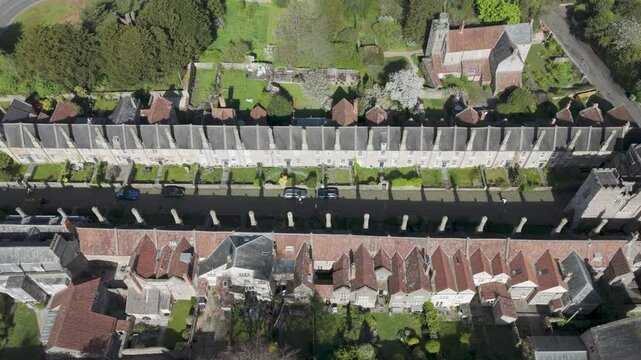 Aerial orbit of medieval Vicars&rsquo; Close showing uniform stone terrace, tall chimneys and cobbled lane aligned toward Wells Cathedral, exemplifying preserved heritage streetscape and historic living