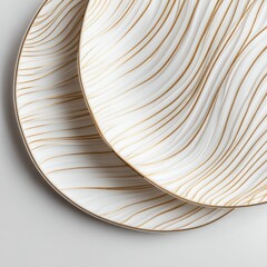 Two white ceramic plates with embossed gold wavy lines, subtly overlapping, rest on a light gray background