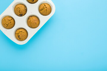 Fresh pumpkin muffins with raisins in white silicone cupcake form on light blue table background. Pastel color. Closeup. Sweet snack. Empty place for text. Top down view.
