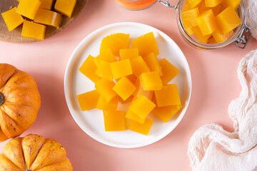 Sweet homemade dessert: pumpkin marmalade. Delicious pumpkin marmalade on a white plate on a pink background. View from above. Close-up