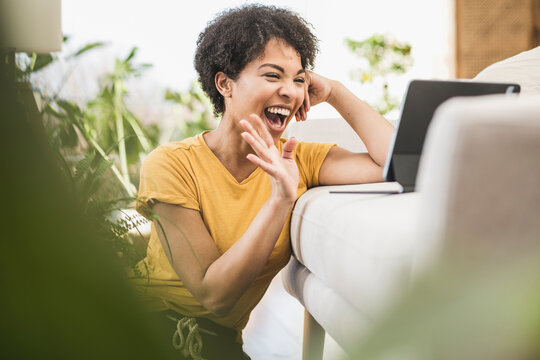 Cheerful woman waving hand to video call on digital tablet while sitting at home