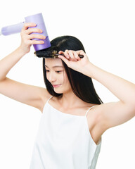Asian girl using comb and hair dryer to blow her hair