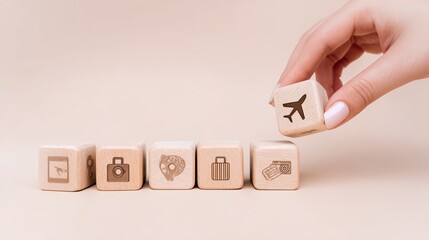 A hand with natural nails picks up a wooden cube displaying an airplane symbol. The other cubes in the row showcase various travel-themed icons. The setting is neutral and minimalistic