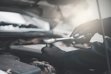 Close-up of professional car mechanic fixing a car. Mechanic is fixing the engine. Mechanic is wearing gloves and using a wrench.