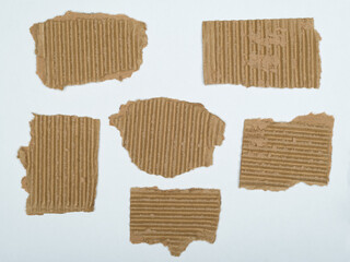 Six irregularly shaped pieces of brown corrugated cardboard are scattered on a white surface