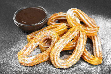 Traditional spanish dessert churros, fried dough pastry dusted with powdered sugar and chocolate sause on black background. Street food, sweet snack, homemade dessert.