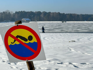 A sign prohibiting swimming over a frozen lake in winter, on a snow-covered beach