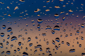 Raindrops on the window against the background of the setting sun. Background with glass and drip...