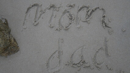 Words “Mom and Dad” written on sand, symbolizing love, family, and heartfelt beach memories.