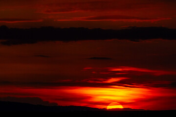 Golden-red sunset casting a warm glow through textured clouds. A perfect balance of light and shadow at twilight