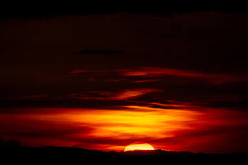 Rich crimson sky streaked with fiery light as the sun dips below the hills. A bold, natural drama