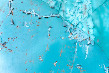 Close-up of cracked and peeling turquoise paint on a rusted metal surface, showing texture and decay in vibrant color contrast.
