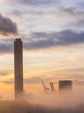 Smoke emitting from chimney near construction site under cloudy sky