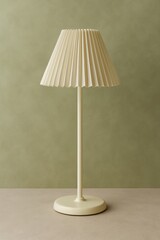 Obraz premium Cream-colored pleated lampshade table lamp with a slender stem and round base against a sage green wall.