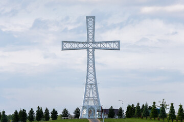 A wide view of the hilltop religious complex with giant cross, visitors and paths reflecting faith, architecture and landscape blending in unity