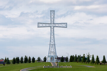 People walk a winding path toward the massive hilltop cross, surrounded by manicured lawns and religious symbolism in the Ukrainian countryside