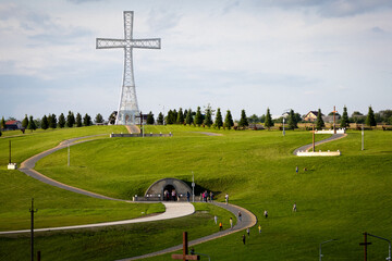 People climb the gently curved path up the hill towards the towering cross, passing stations of the cross and smaller wooden crosses on the way