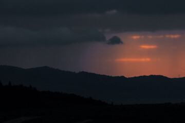 Evening mist rolls over the mountain ridges as clouds catch the last golden rays of sunlight. A surreal, cinematic view perfect for travel or weather-themed content