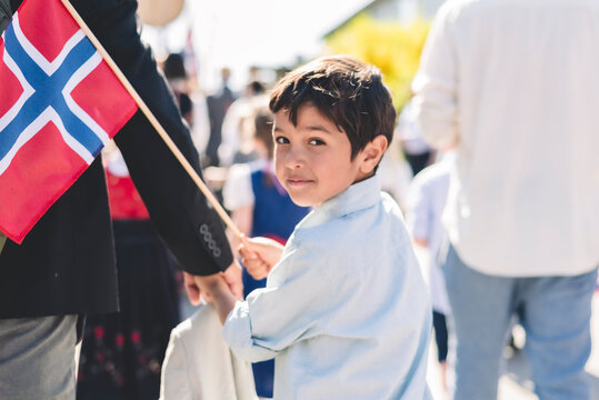 Portrait of cute boy holding Norwegian Flag walking with father in parade, 17 May