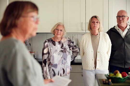 Senior women and man listening to instructions given by friend in kitchen at home