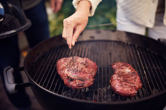 Senior woman checking temperature of meat with digital thermometer on barbecue