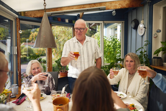 Senior man doing celebratory toast with friends at patio of house - Powered by Adobe