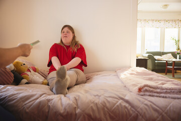 Woman with down syndrome sitting on bed during storytelling session in bedroom at nursing home