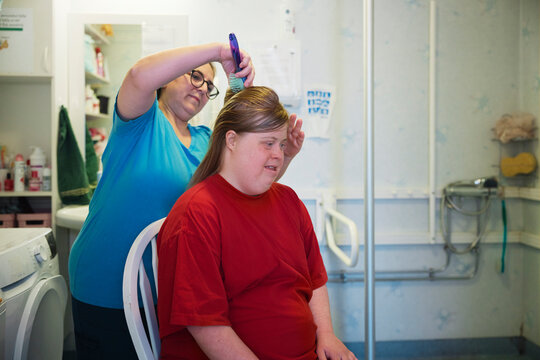 Female nurse combing disabled woman's hair with hairbrush in bathroom at nursing home