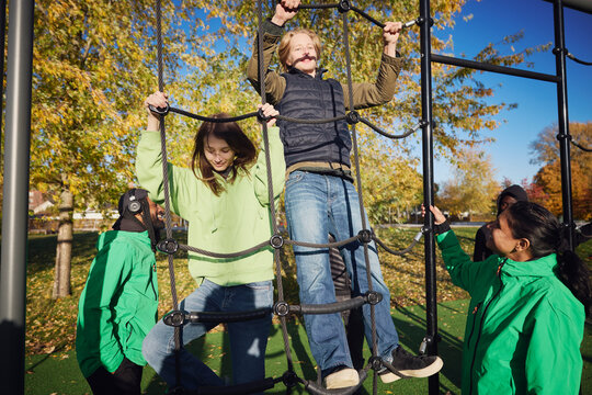 Female coach instructing teenage boy and girl climbing rope in jungle gym