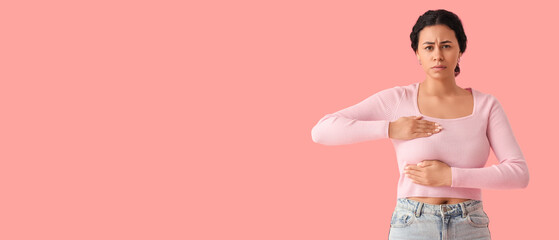 Worried African-American woman checking her breast on pink background. Cancer awareness concept