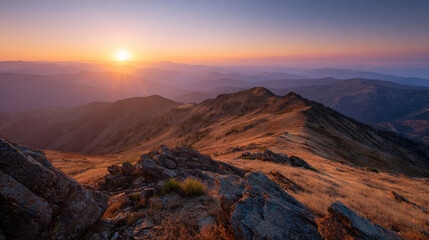 Breathtaking sunset over mountain ridgeline, with sun just below horizon casting warm hues across sky. landscape features rocky terrain and rolling hills, evoking sense of tranquility and awe