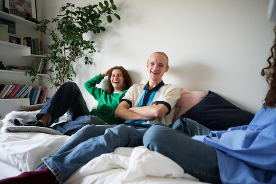 Male and female friends enjoying leisure time sitting on bed at home