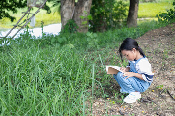 A young girl is sitting in the grass and writing in a notebook.