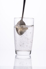 Collagen or medicinal powder is stirred with a spoon in a glass of water on a white background.