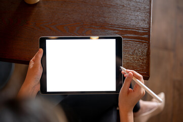Top view close up of hand holding blank screen tablet with a stylus on table in cafe or coffee shop.