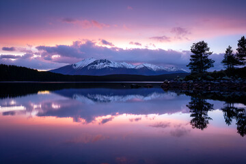 Fototapeta premium Picturesque mountain range reflecting in a serene lake at sunset with a colorful sky and tranquil water, creating a peaceful and idyllic landscape