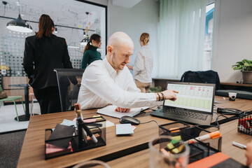 Group of colleagues working together on data analysis, laptops and charts in a modern office environment, fostering teamwork and productivity.