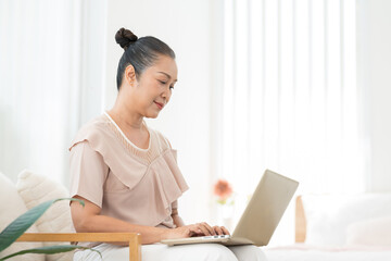 Asian elderly woman happy and smile while using laptop computer, working or shopping online from home