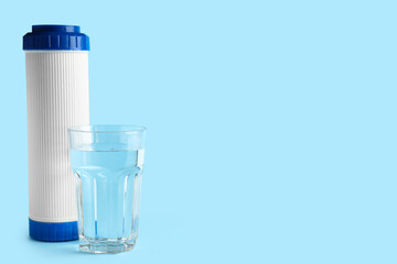 Glass of liquid and water filter cartridge on blue background