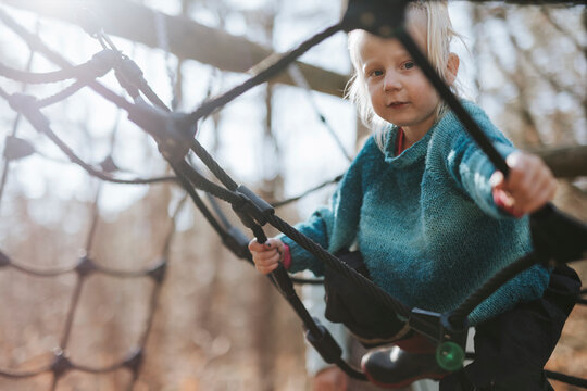 Portrait of cute blond girl playing on ropes at jungle gym
